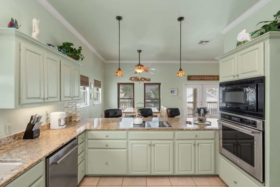 Kitchen with seafoam cabinets, granite countertops, pendant lights, and bar seating