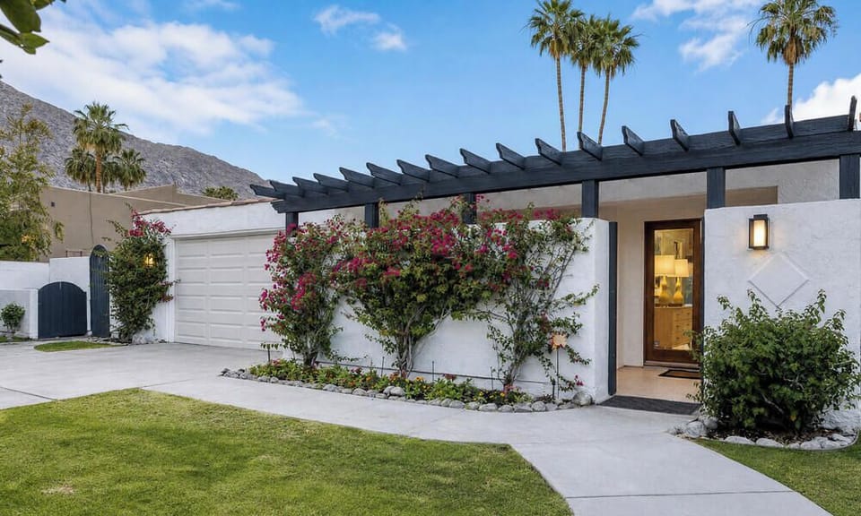 A modern desert retreat surrounded by lush landscaping and towering palms, set against mountain views in a peaceful Palm Springs neighborhood.