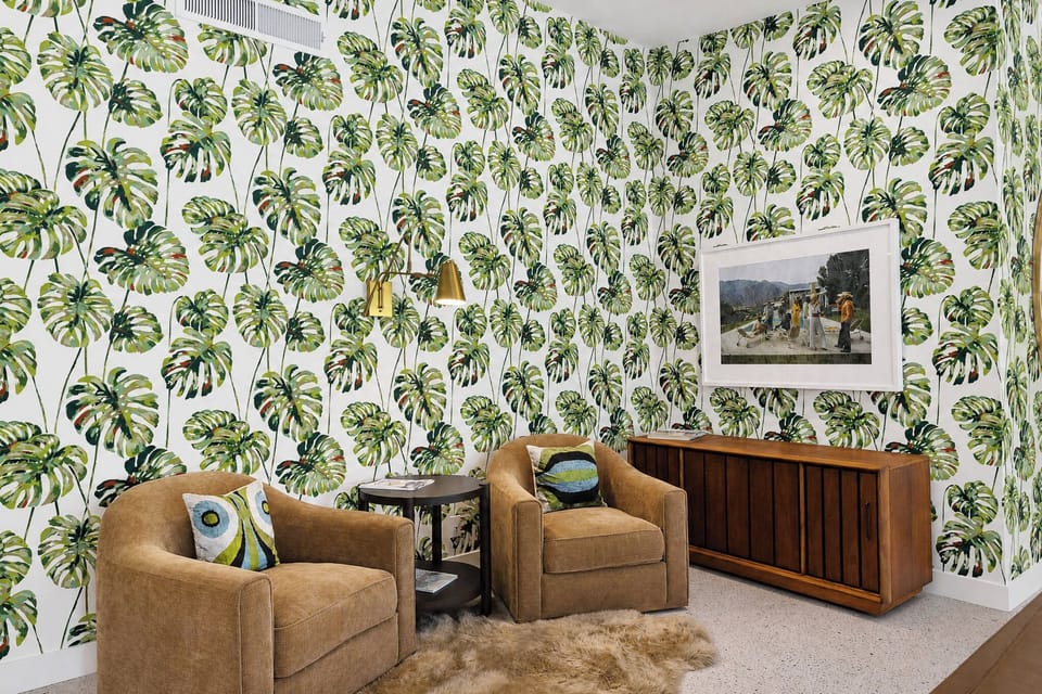Relax in your stylish living space featuring lush botanical wallpaper, cozy armchairs, and warm wood tones that create a tropical, inviting atmosphere for unwinding after exploring.