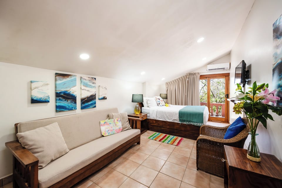 Master bedroom in Playa Langosta, Tamarindo Costa Rica vacation rental with queen-sized bed, TV, futon lounge, and spacious design. Elegant retreat with patio access, offering ocean breeze, tropical comfort, and relaxing space for family vacations.