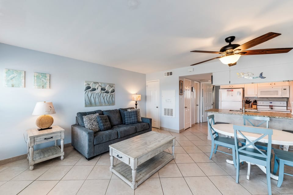 Relax in your coastal-inspired living space featuring comfortable seating, tile floors, and an open kitchen layout perfect for vacation dining.