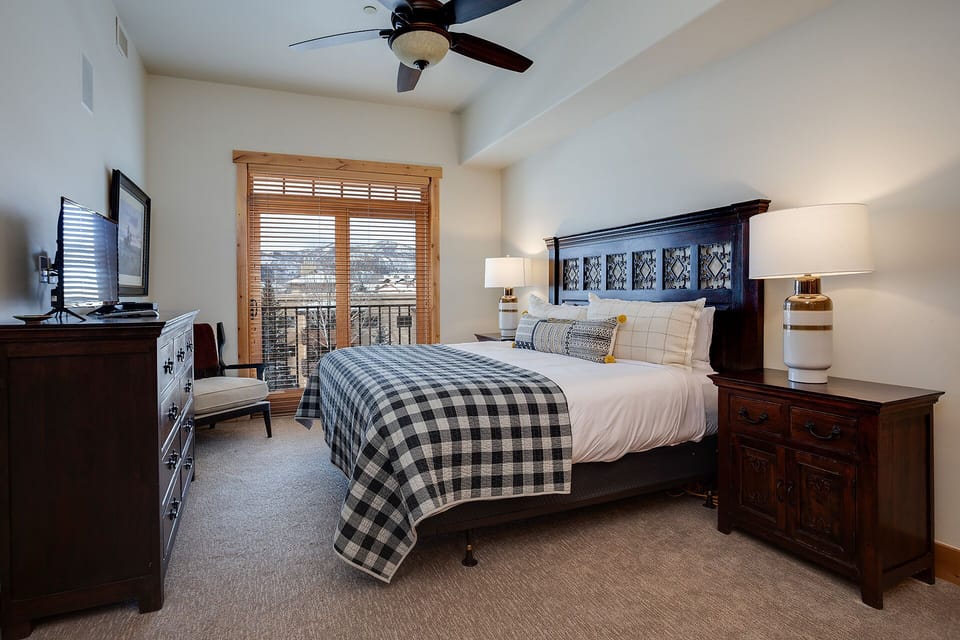 Unwind in your cozy bedroom featuring rich wood furnishings, soft plaid bedding, and peaceful mountain views from your private balcony.
