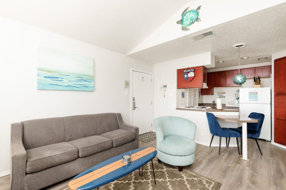 Unwind in your coastal-inspired living space with ocean artwork and a swivel chair, flowing into your full kitchen perfect for morning coffee.