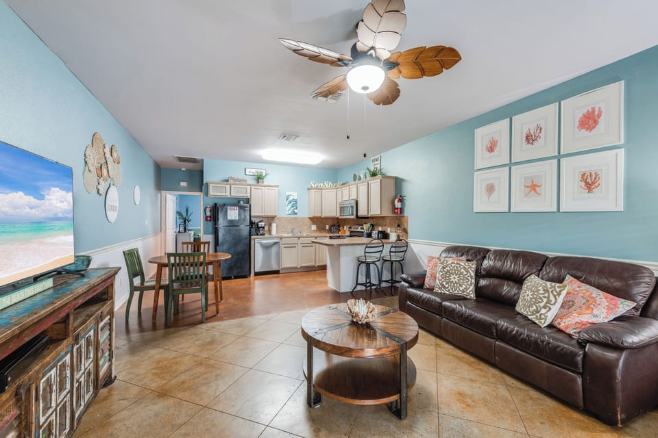 Unwind in your coastal-themed living space with tropical ceiling fan, comfortable leather sleeper sofa, and ocean-inspired artwork creating the perfect beach getaway atmosphere.