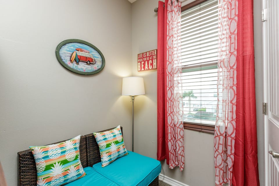 Relax in your cozy reading nook with cheerful beach-themed decor, tropical pillows, and warm natural light streaming through coral curtains.