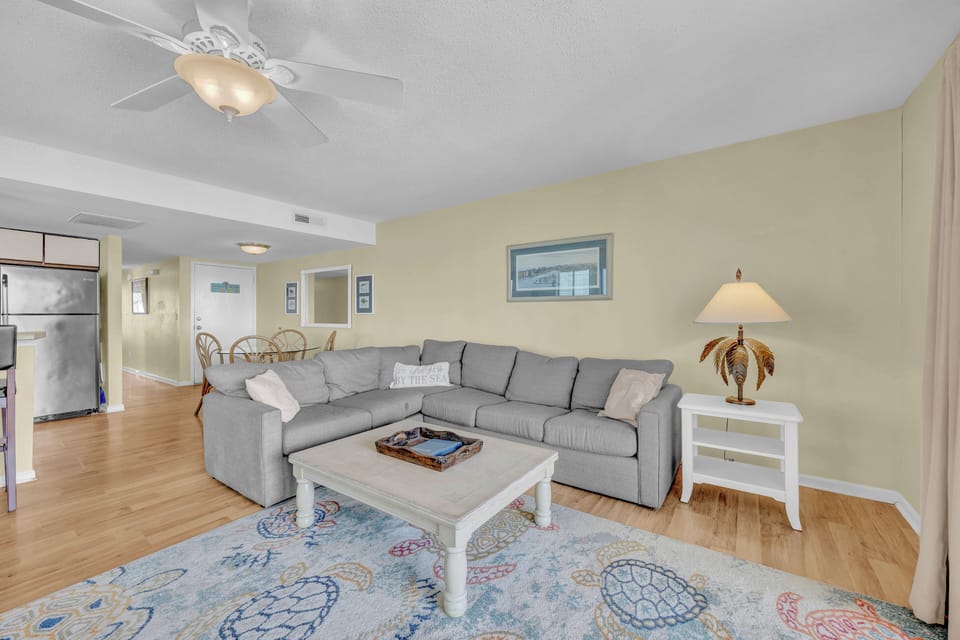 Unwind on a plush sectional in your bright, coastal-inspired living space with open views to the dining area and kitchen—perfect for family time or relaxation after beach adventures.