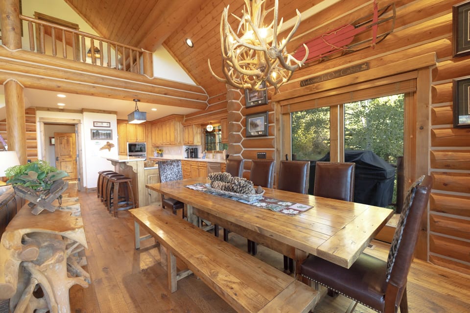 Gather around this stunning rustic dining table where memories are made! The antler chandelier casts a warm glow over your group meals while natural light streams through large windows.