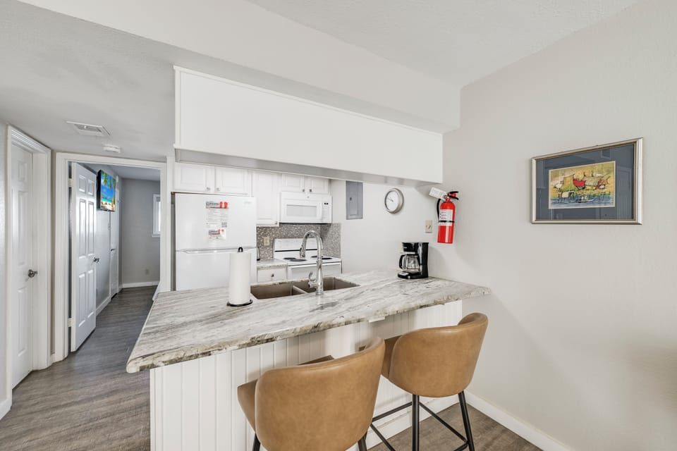 Gather at the bright breakfast bar with gorgeous granite countertops, where your morning coffee feels extra special. The fully-equipped kitchen makes meal prep effortless, with modern appliances and sleek white cabinetry at your fingertips.