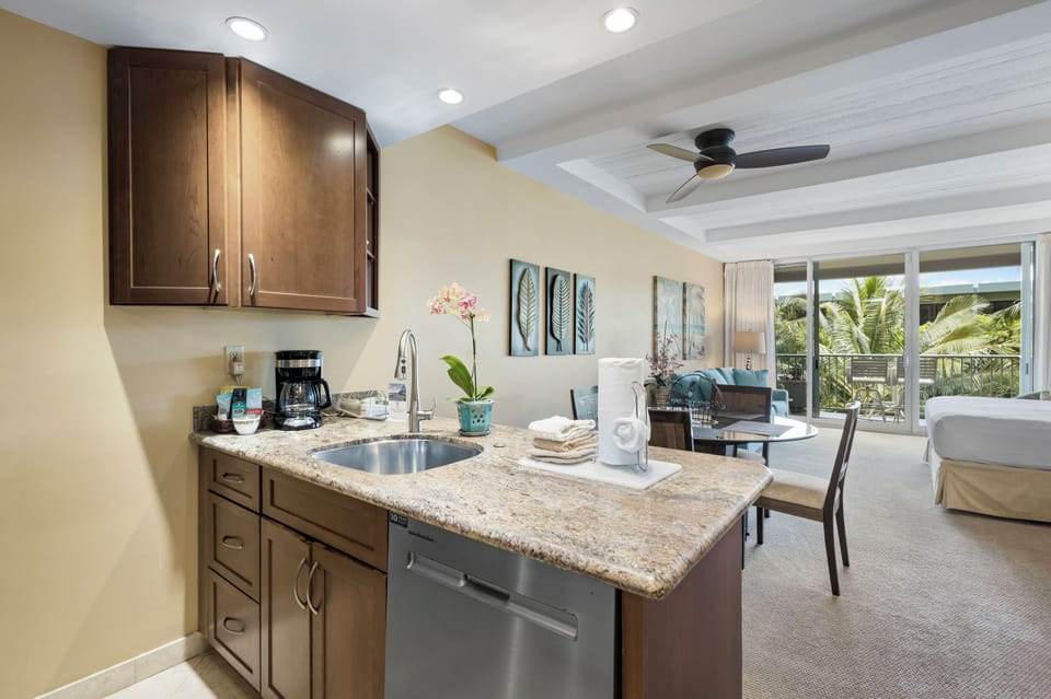 Your bright studio features a full kitchenette with granite counters and stainless appliances, flowing seamlessly into a comfortable living space with tropical garden views from your private balcony.