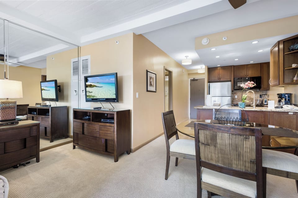 Relax in your open-concept living area with a fully-equipped kitchen, cozy dining for four, and entertainment essentials including a flatscreen TV—all bathed in warm, welcoming natural light.