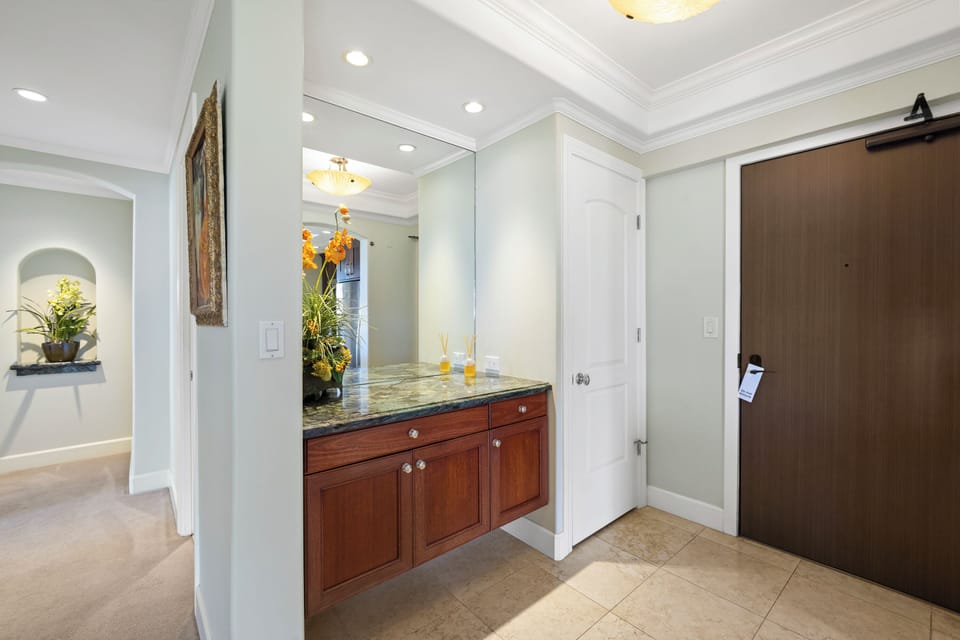 Step into your private retreat, where elegant crown molding and recessed lighting frame a stylish vanity with granite countertop. Fresh plants and warm wood tones create a welcoming ambiance the moment you arrive.