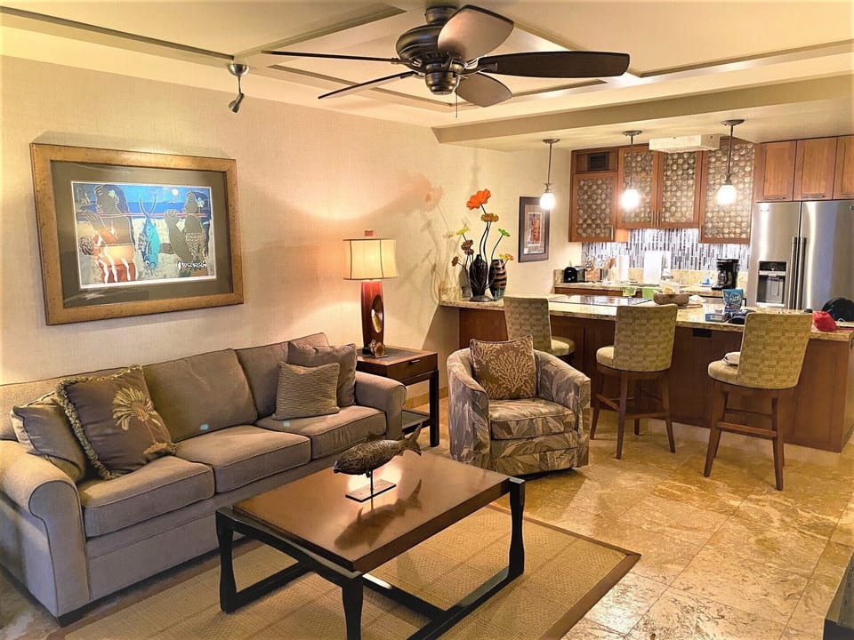 Settle into your open-concept living space where warm tropical details meet modern comfort—cozy seating, a fully equipped kitchen, and ceiling fan breezes await your arrival.