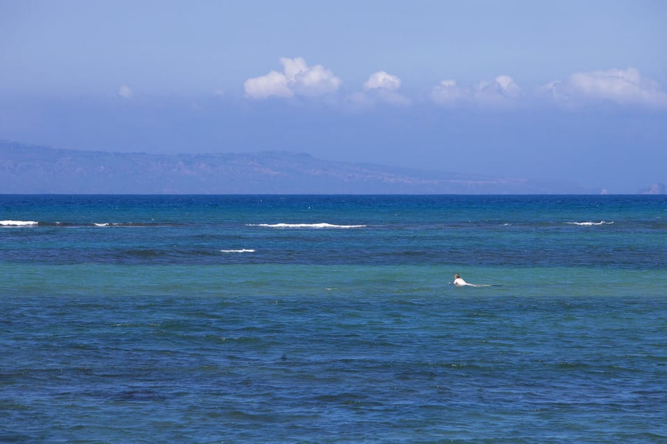 Tranquil coastal waters meet distant mountain ranges under a soft blue sky, showcasing the scenic seaside location of the property.