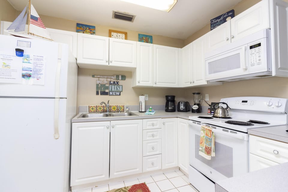 Tile backsplash with floral patterns accents the double stainless steel sink beneath white cabinetry.