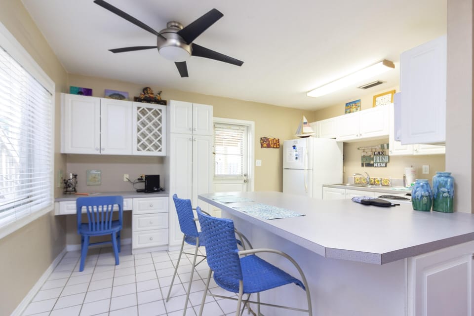 White cabinetry and a large peninsula with blue woven bar stools define the kitchen space.