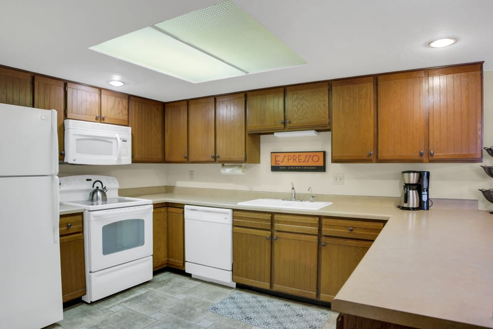 Park Station 122's kitchen has wood cabinets, white appliances, cream counters, white walls, and grey tiled floors.