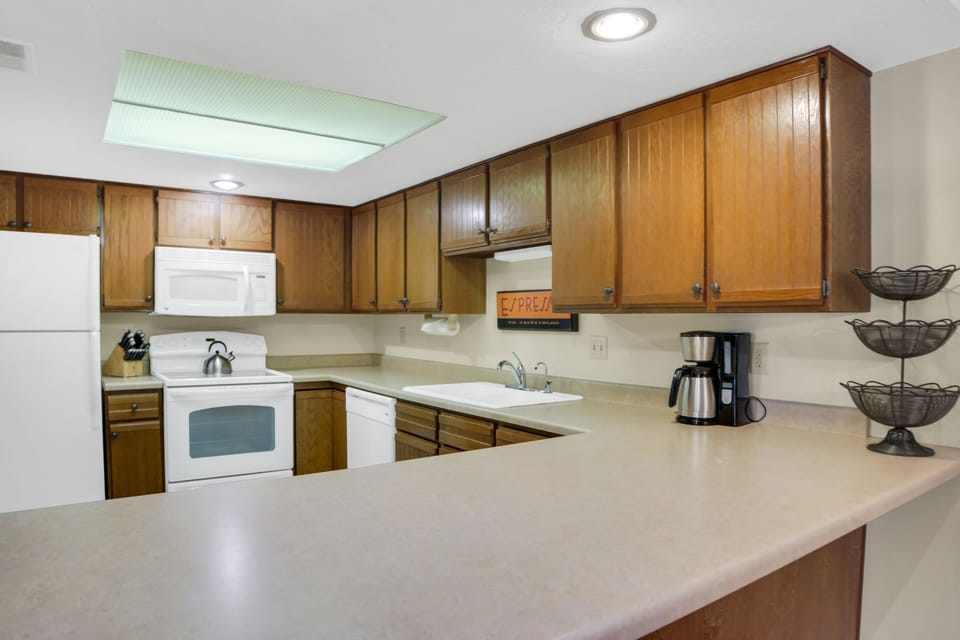 Park Station 122's kitchen has wood cabinets, white appliances, cream counters, white walls, and grey tiled floors.