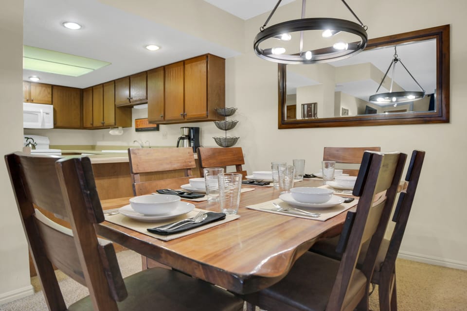 Park Station 122's dining room has a wood table, 6 chairs and place settings, black circular chandelier, and next to kitchen.