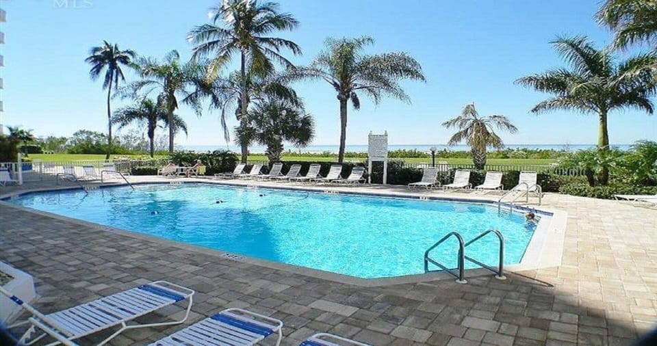 Heated pool surrounded by tables and lounge chairs overlooking the beach.