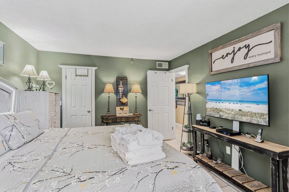 Unwind in your serene bedroom with calming sage walls, a plush bed, and a smart TV streaming coastal views—your peaceful retreat awaits.