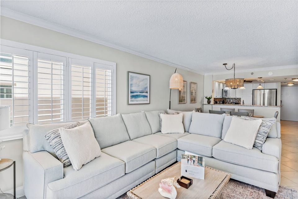 Sink into this plush sectional sofa where natural light streams through elegant shutters, creating your perfect spot to unwind after exploring.