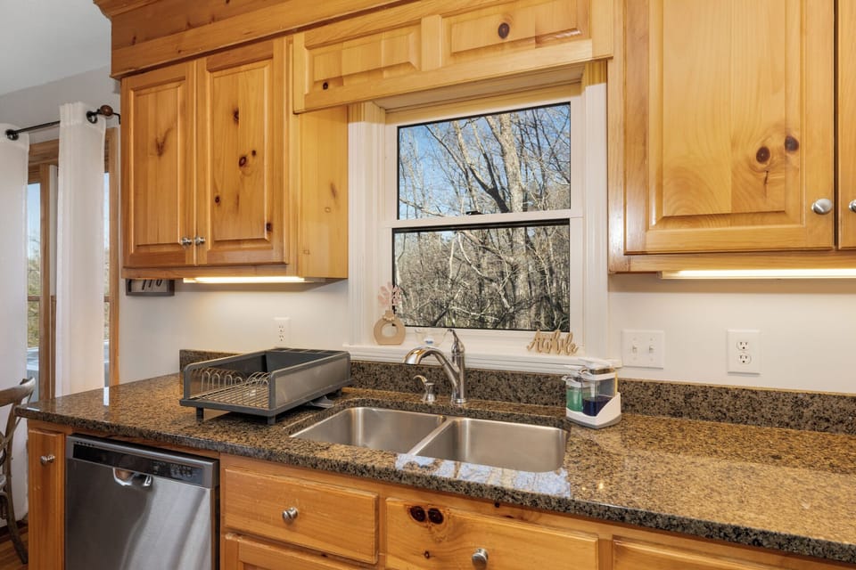 Prepare delicious meals in your fully equipped kitchen featuring warm wood cabinets, granite countertops, and modern appliances with lovely forest views.