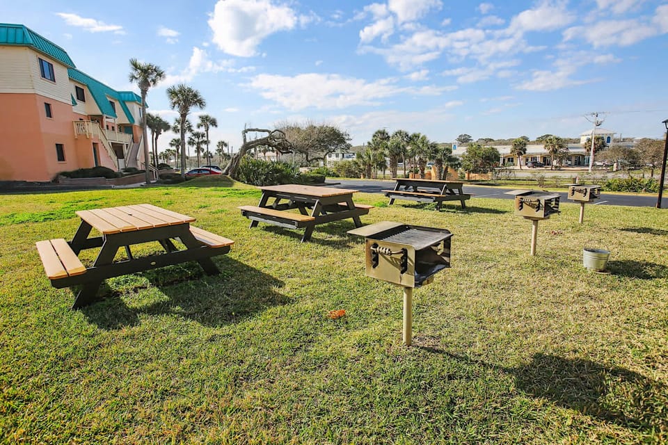 - Outdoor picnic area with grills and tables perfect for family barbecues  
- Open grassy space designed for gatherings and meals under the sunny sky  
- Convenient setup adds fun community vibes to your coastal vacation stay  
