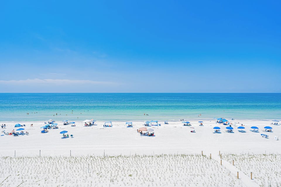 White sand stretches toward clear turquoise waters beneath endless blue skies. Spend your days relaxing under an umbrella or wading into the gentle waves, surrounded by pure coastal beauty.