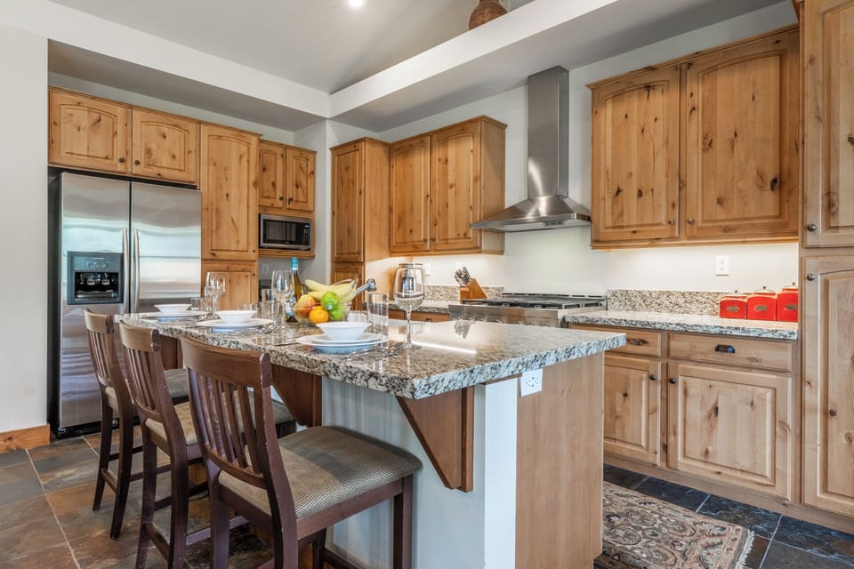 Picture yourself preparing meals in this inviting kitchen featuring warm knotty-pine cabinetry, granite countertops, stainless appliances, and an island with bar seating perfect for casual dining or morning coffee.