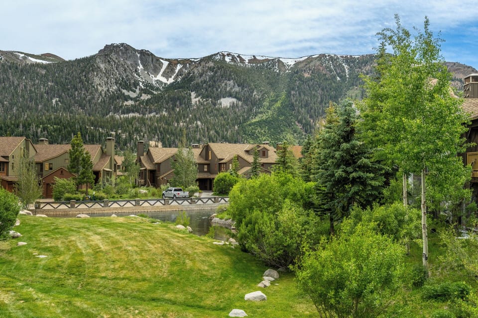 Mountain retreat nestled in a scenic valley with snow-capped peaks, lush greenery, and a tranquil creek flowing through the property grounds.