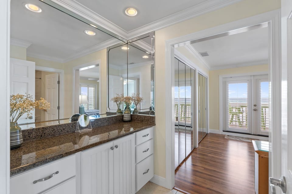 Pamper yourself in this elegant bathroom featuring granite counters, expansive mirrors, and beautiful natural light from the adjoining balcony.