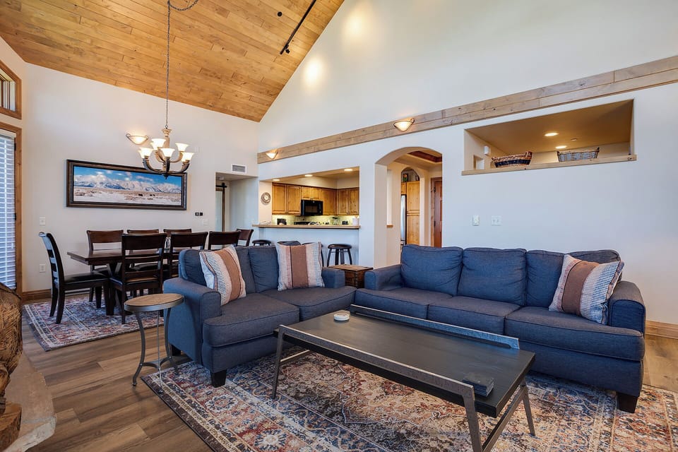 Relax in your spacious living area with soaring wood ceilings, plush blue sectional, and open kitchen—perfect for memorable evenings together.