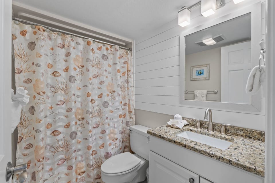 Freshen up in your coastal-themed bathroom with granite countertops, modern lighting, and charming seashell shower curtain.