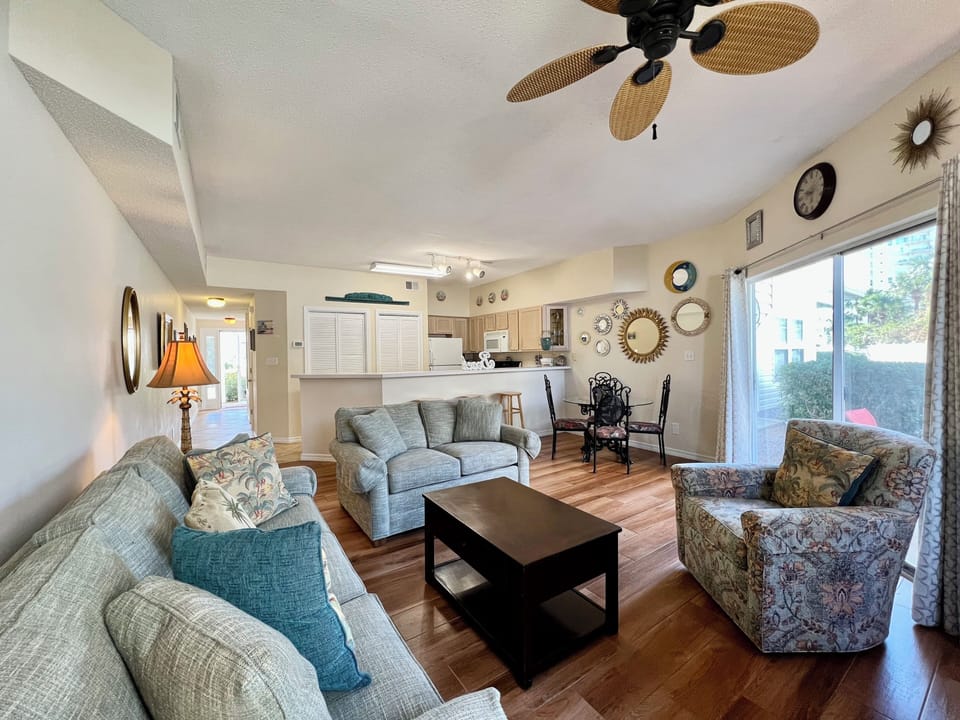 Relax in your spacious living room with comfortable seating, tropical ceiling fan, and open-concept design that flows seamlessly into the kitchen.