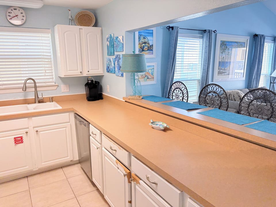 Your bright, beachy kitchen flows into the dining area where coastal artwork and ocean blues create a serene space for cooking and gathering.