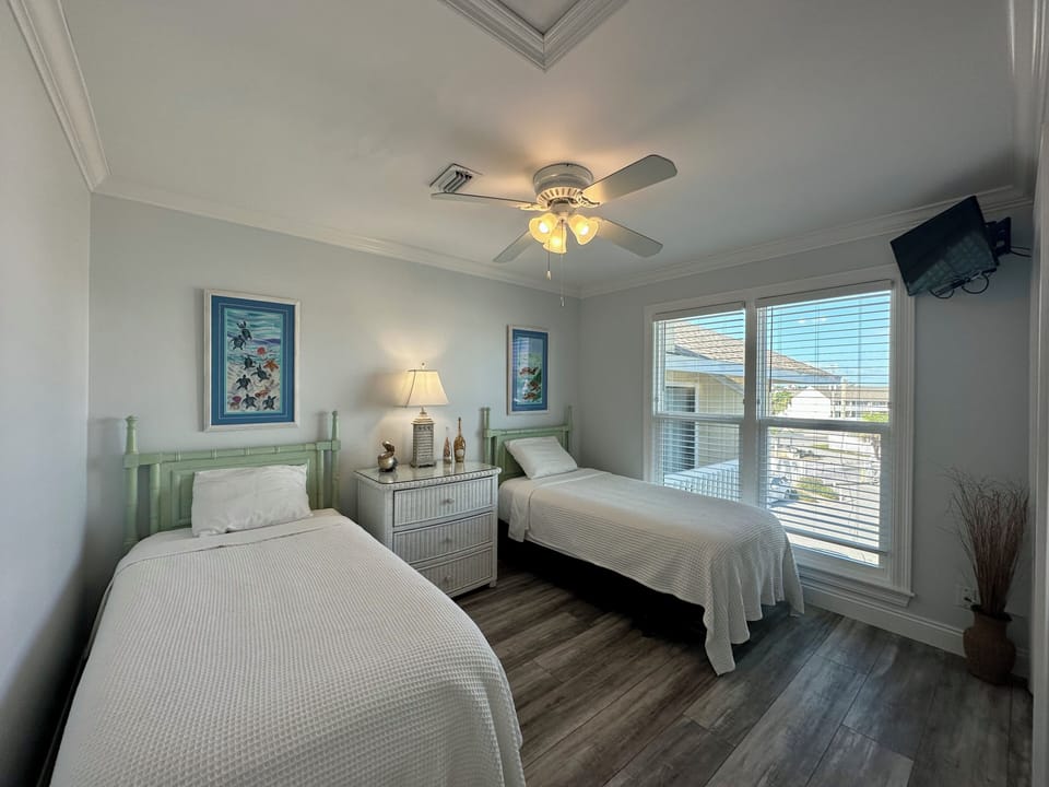 Your peaceful twin bedroom features crisp linens, gentle ceiling fan, and natural light streaming through large windows for restful nights.