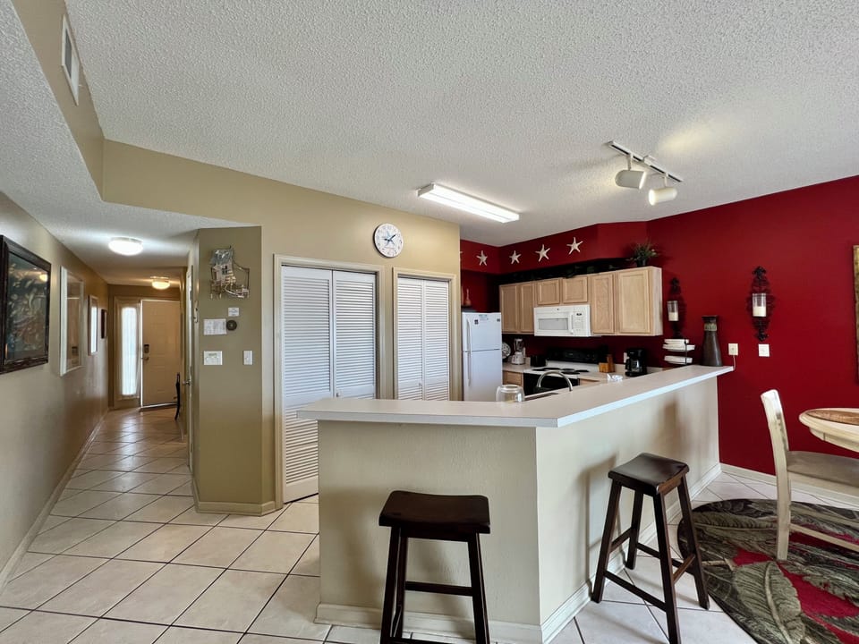 Your bright kitchen invites culinary adventures with its breakfast bar seating and warm red accent wall creating a welcoming space.