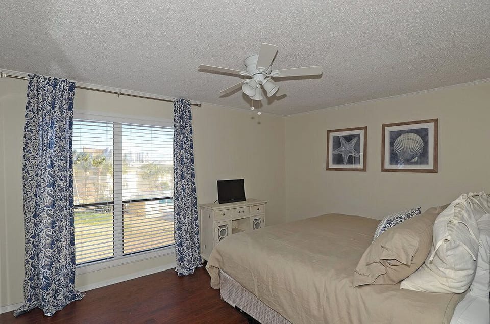 Relax in your serene bedroom featuring coastal decor, ceiling fan, and peaceful city views through the large windows.
