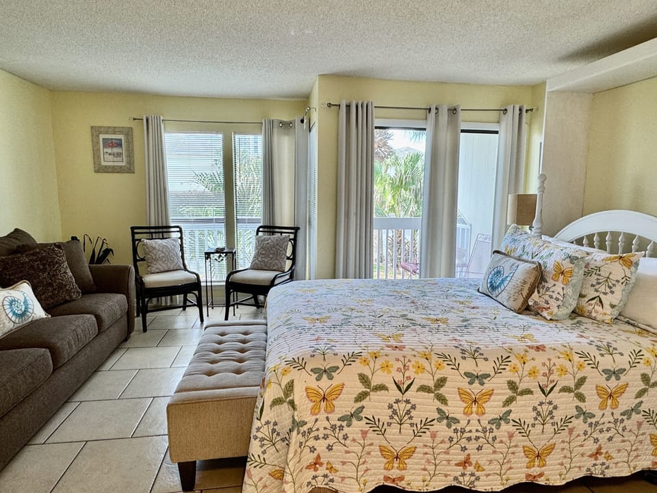 Your bright bedroom features tropical views through sliding doors, cozy seating, and cheerful floral bedding for peaceful rest.
