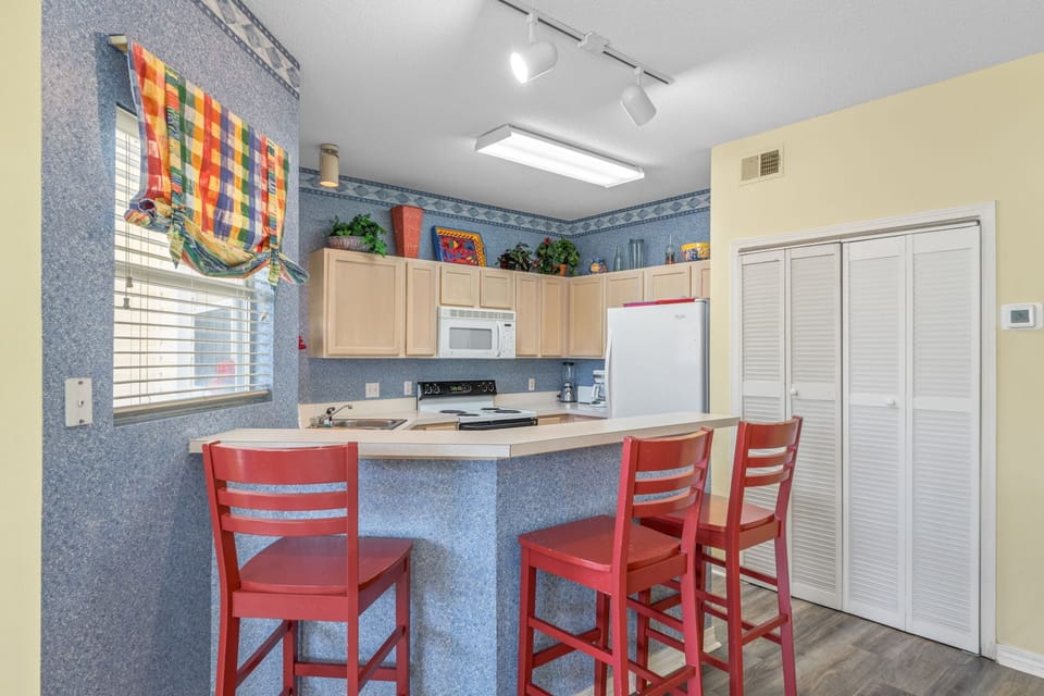 Your bright kitchen features cheerful red stools, full appliances, and a cozy breakfast bar perfect for morning coffee or evening meals.