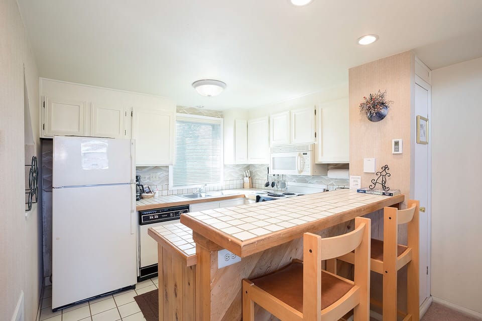 Cook your favorite meals in this bright, fully-equipped kitchen featuring white cabinets, tile countertops, and a cozy breakfast bar.