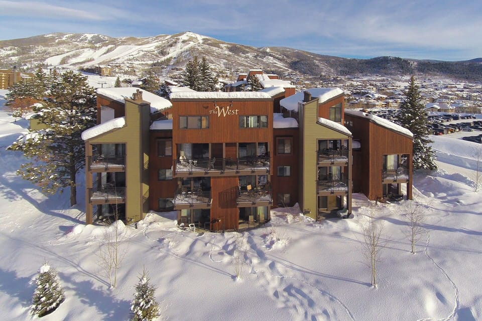Modern mountain lodge nestled in pristine winter landscape with snow-covered peaks and valley views stretching beyond.