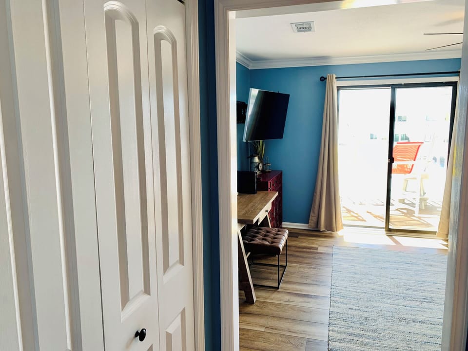 Relax in your bright living space with stylish blue accent walls, flat-screen TV, and private balcony access for peaceful moments outdoors.