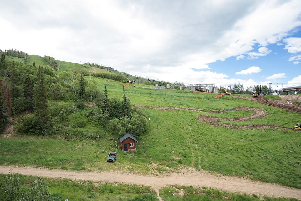 A secluded mountain cabin nestled in rolling green hills with ski slopes and forest surroundings.