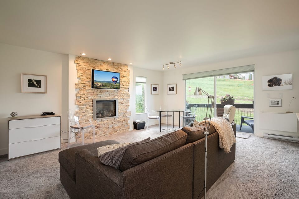 Unwind in your stylish living room featuring a cozy fireplace, modern furnishings, and peaceful garden views through expansive windows.