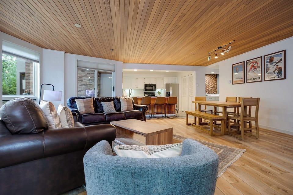 Relax in your stylish open-plan living space featuring warm wood ceilings, cozy leather seating, and a fully equipped kitchen perfect for gathering.