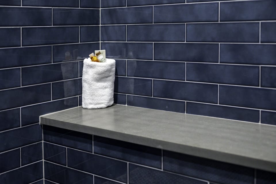 A sleek bench and fluffy towel await in your stylish tiled shower, where modern design meets your everyday comfort.