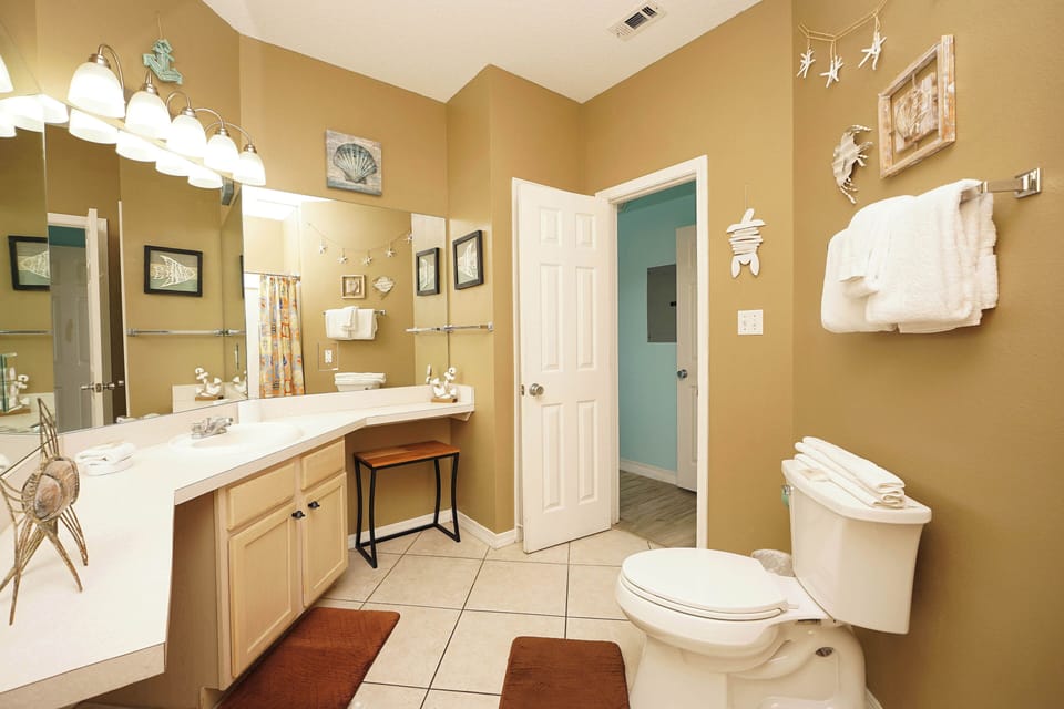 Freshen up in your spacious bathroom featuring dual vanities, bright lighting, and coastal-themed decor that creates a relaxing retreat.
