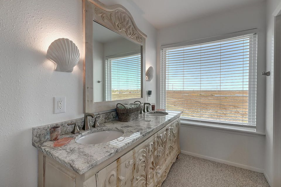Pamper yourself in this elegant bathroom with coastal charm—marble counters, shell accents, and stunning desert views create your perfect retreat.