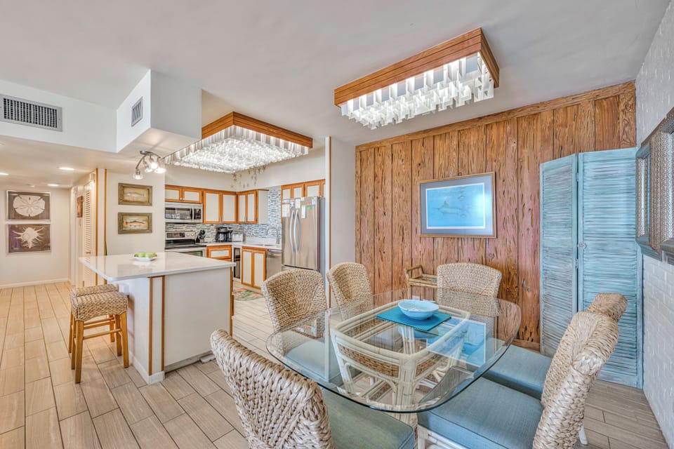 Relax in your coastal-inspired living space where warm wood meets comfortable wicker seating beneath stunning crystal chandeliers.